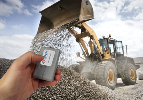 hand-holding-zonesafe-tag-infront-of-shovel-loader-tipping-aggregate
